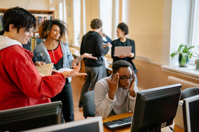 A group of diverse students engaged in study at a library with computers and books.