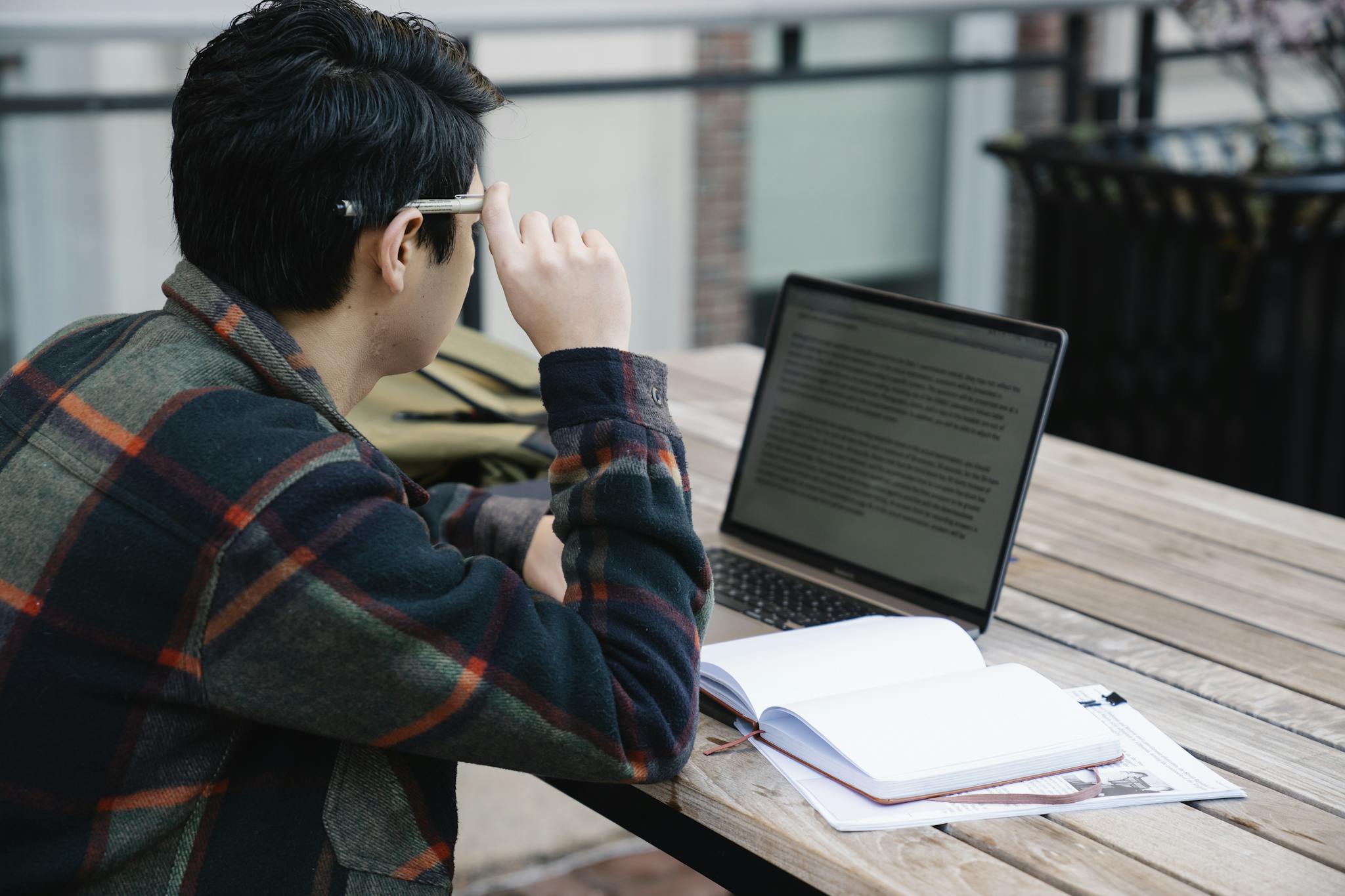 A student studies with a laptop and notebook outdoors, reflecting modern learning.